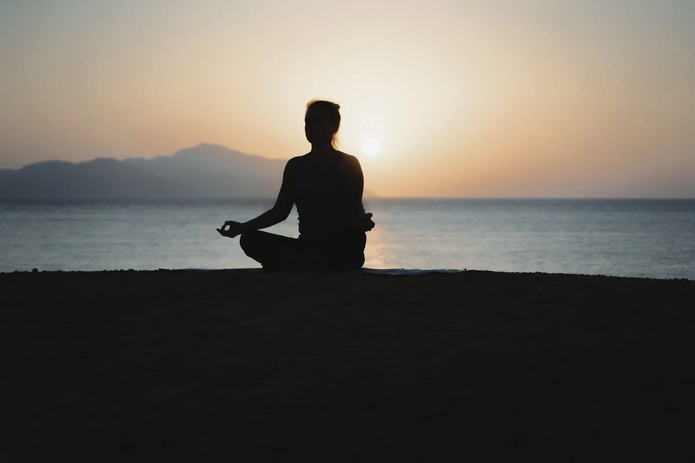 Silhouette meditating on the beach at sunset