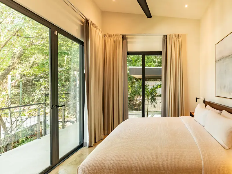 Bedroom with corner glass doors opening to a jungle balcony