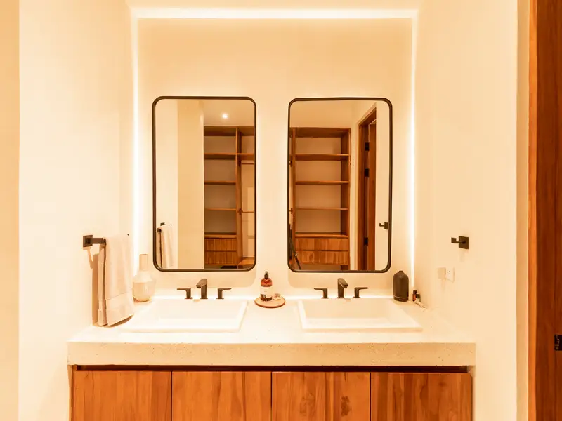 Double-vanity bathroom with backlit mirrors and teak cabinetry