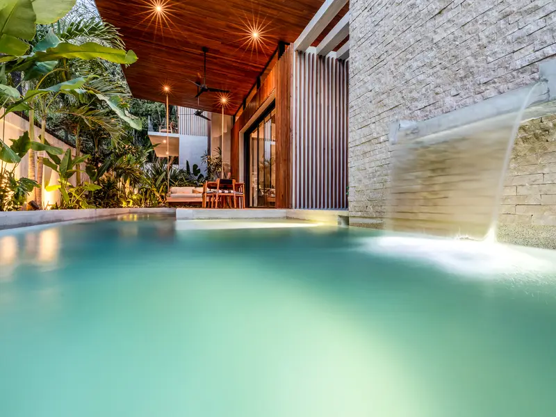 Pool waterfall lit at night with the terrace glowing behind