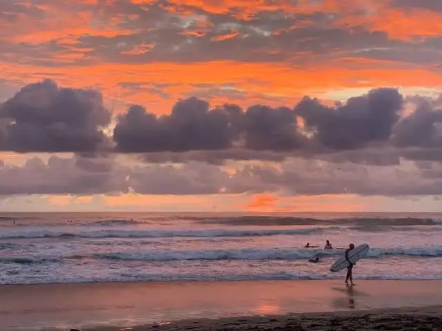 Surfers heading out at sunset on Playa Guiones' sandy-bottom beach